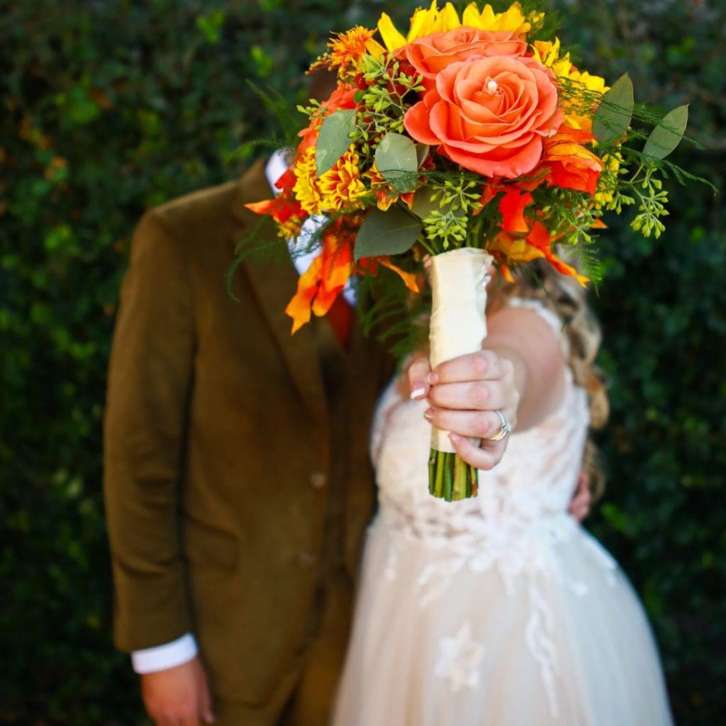 Wedding photography of couple behind Fall Floral Bouquet in Fall Wedding Venue